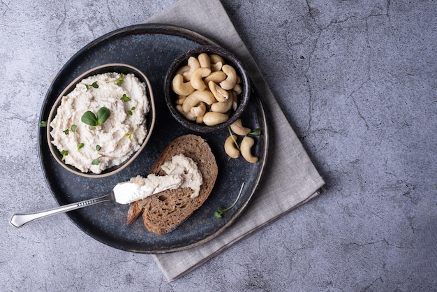 Fromage de cajou végétalien et une tranche de pain sur une assiette grise, fromage à la crème sain à base de noix fermentées.