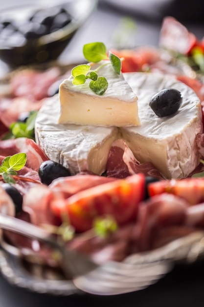 Photo fromage camambert de prosciutto ou jambon de coppa tomates olives et origan herbes.