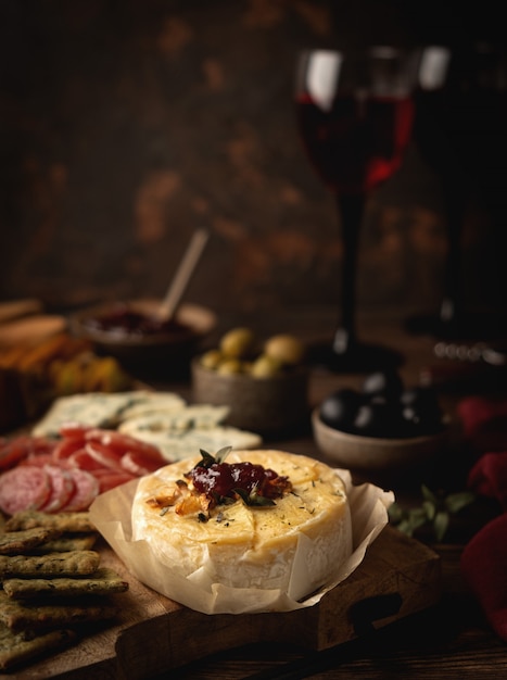 Fromage camembert au four avec confiture, saucisse, fromage bleu, olives et collations, sur une planche de bois, verres à vin rouge