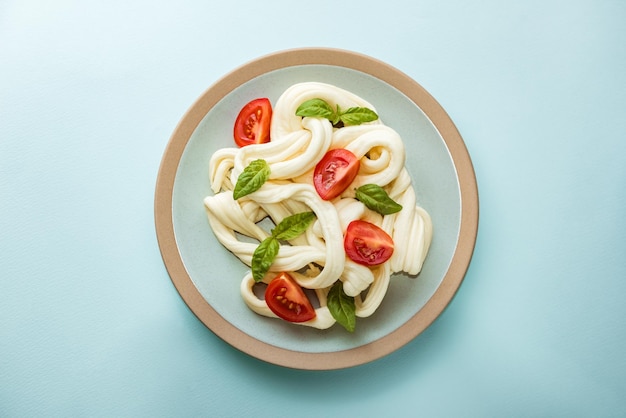 Le fromage Cecil fibreux blanc traditionnel se trouve sur une assiette. Le fromage est décoré de tomates mûres et de basilic, vue de dessus