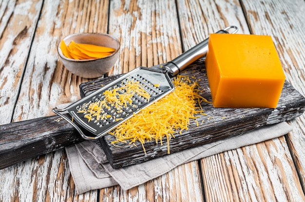 Fromage cheddar râpé sur une planche à découper en bois. Fond en bois blanc. Vue de dessus.