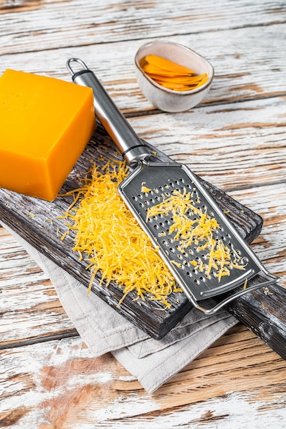 Fromage cheddar râpé sur une planche à découper en bois. Fond en bois blanc. Vue de dessus.