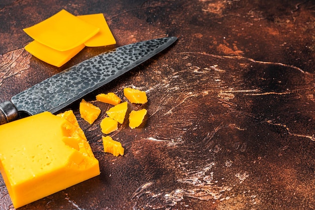 Fromage cheddar tranché sur une table de cuisine avec un couteau. fond sombre. Vue de dessus. Espace de copie.