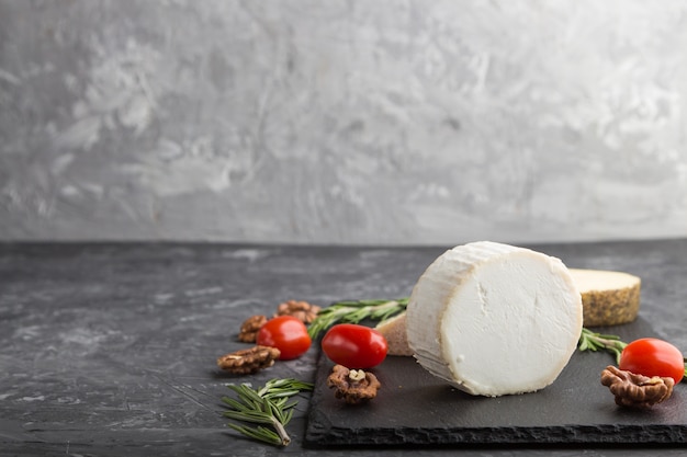 Fromage de chèvre et différents types de fromage aux tomates sur ardoise noire sur fond de béton noir