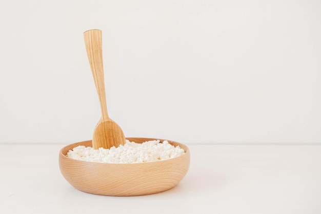 Fromage cottage dans une assiette en bois avec une cuillère sur un fond blanc