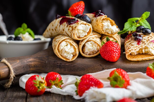 fromage cottage enveloppé dans des crêpes, avec des baies, de la menthe, de la confiture, un arrière-plan sombre et isolé