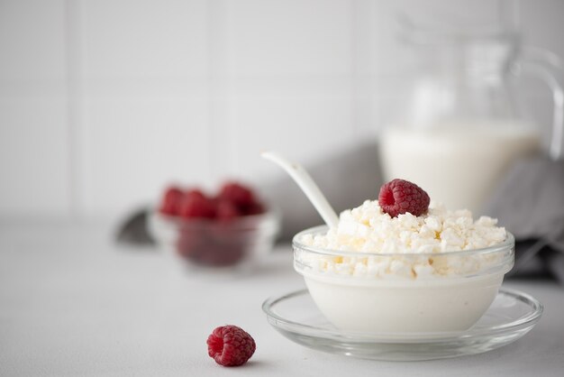 Fromage cottage fait maison avec du lait et des framboises dans un bol en verre sur un tableau blanc