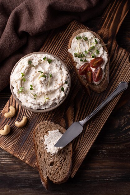 Fromage à la crème de cajou étalé sur une tranche de pain sur une table en bois sombre, produits végétaliens fermentés, concept d'alimentation saine.