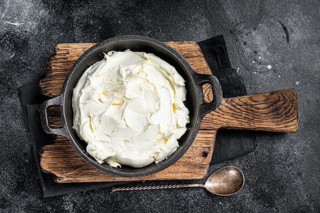 Fromage à la crème mascarpone dans une poêle pour tiramisu. Fond noir. Vue de dessus.