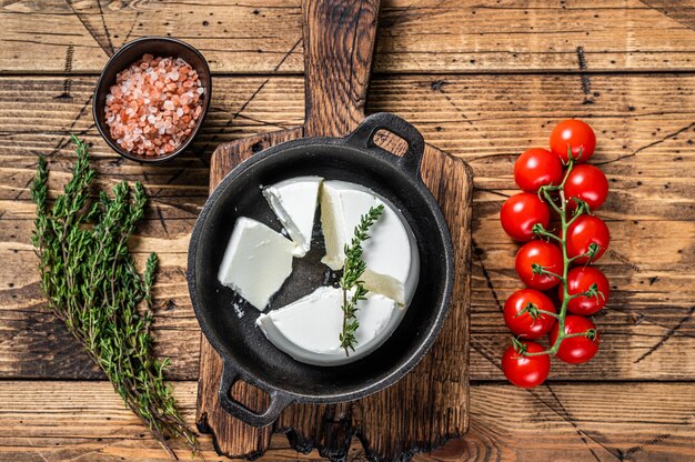 Fromage à la crème Ricotta frais dans une poêle avec basilic et tomate. fond en bois. Vue de dessus.