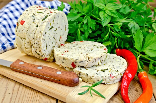 Fromage fait maison aux herbes, épices et poivre, couteau, persil, romarin, serviette sur planche de bois