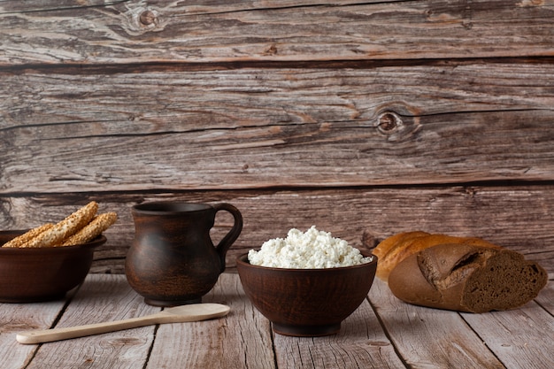 Fromage frais dans un bol en bois avec une cuillère, pot de crème sure sur un bois