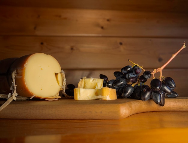 Fromage fumé grec traditionnel Metsovone sur une planche de bois avec des raisins et des kakis en Grèce