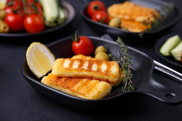 Fromage halloumi grillé dans une poêle noire avec olives tomates concombres thym et citron Fromage traditionnel de la Méditerranée orientale Fond noir mise au point sélective gros plan