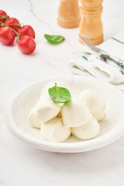 Fromage mozzarella au basilic dans une assiette en céramique blanche et cerise tomate sur fond de pierre d'ardoise