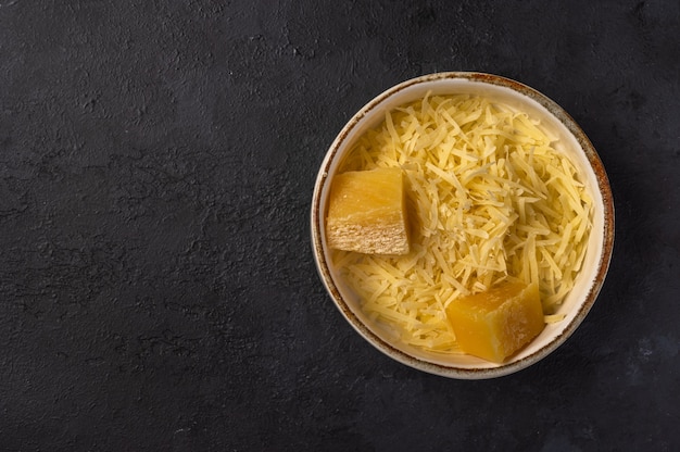 Fromage parmesan râpé et deux morceaux dans un bol en céramique blanche