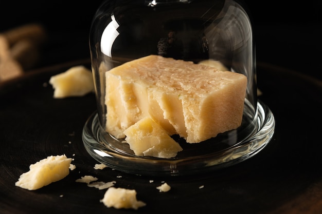 Fromage parmesan tranché avec morceaux ébréchés, recouvert d'un bocal en verre, sur fond sombre