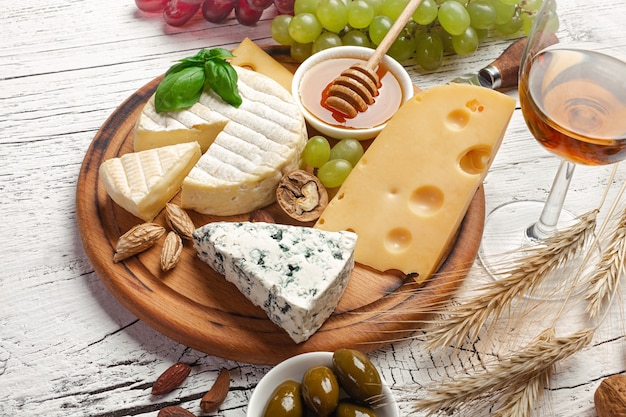 Fromage, raisin, miel et noix sur planche à découper et table en bois blanc. Vue de dessus.