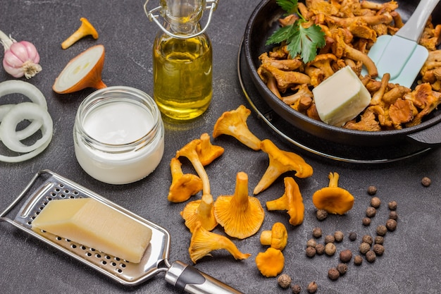 Fromage sur râpe, girolles crues d'oignons hachés sur table. Girolles frites à la poêle. Fond noir. Vue de dessus