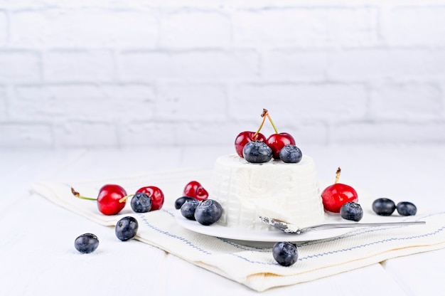 Fromage ricotta frais avec des cerises de myrtilles sur une table en bois blanche. Mur de briques sur fond