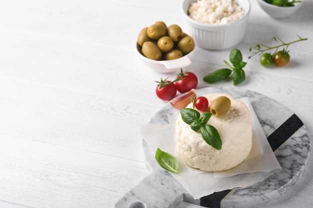 Fromage ricotta Fromage ricotta fait maison avec des tomates à l'ail au basilic et des olives vertes sur papier parchemin et se tenir sur de vieux carreaux beiges arrière-plan Cuisine italienne Mise au point sélective