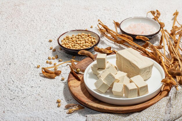 Photo fromage de tofu frais avec des morceaux de cube de soja ingrédient sain pour un style de vie végétalien support moderne tendance lumière dure ombre sombre fond de plâtre espace de copie plat