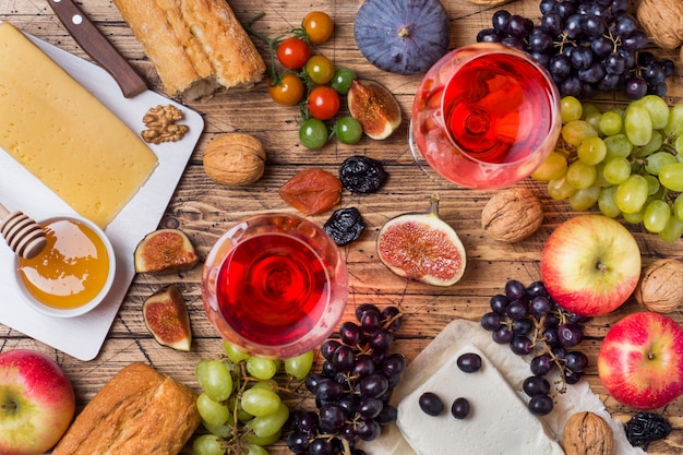 Fromage, vin, baguette, figues, raisins, miel et collations sur le plateau en bois rustique.