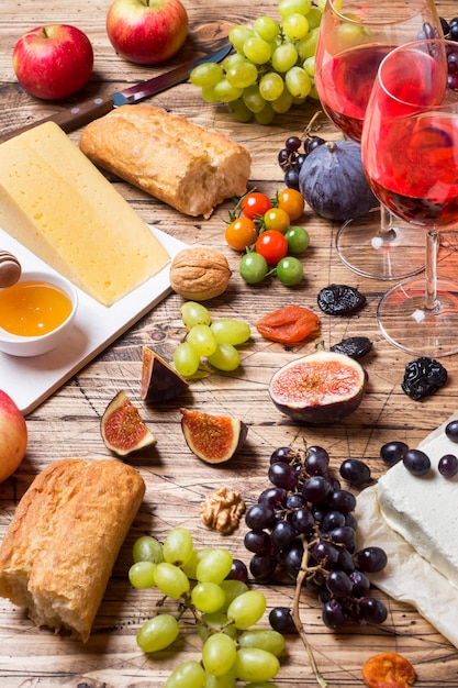 Fromage, vin, baguette, figues, raisins, miel et collations sur le plateau en bois rustique.