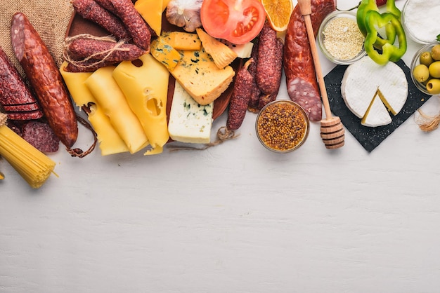 Fromages assortis et saucisses et légumes traditionnels sur un fond en bois blanc. Fromage brie, fromage bleu, gorgonzola, fuete, salami. Cuisine traditionnelle italienne. Espace libre pour le texte. Vue de dessus.