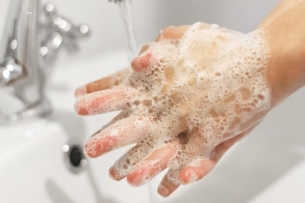 Frotter les doigts Se laver les mains avec un savon antibactérien selon la technique appropriée sur fond d'eau qui coule dans une salle de bain blanche Prévention du coronavirus Nettoyage et désinfection