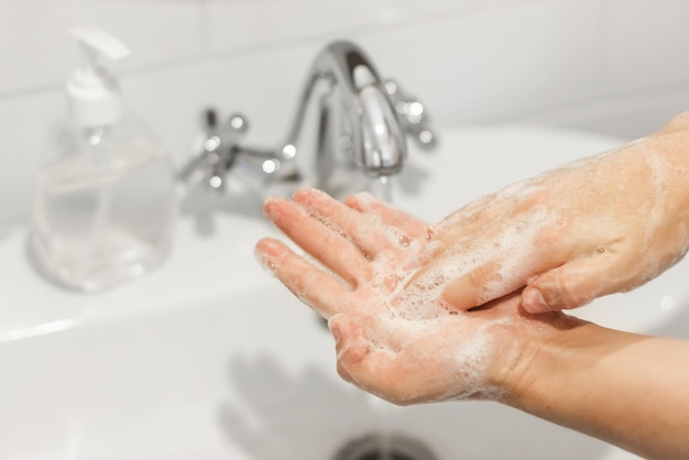 Frotter les paumes se laver les mains avec du savon antibactérien et dans la bonne technique sur fond d'eau qui coule dans la salle de bain blanche Prévention coronavirus Nettoyage et désinfection des mains