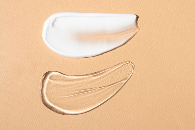 Frottis cosmétiques de gel transparent et de crème blanche sur un gros plan de fond beige