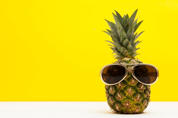 Fruit d'ananas d'été avec des lunettes de soleil sur un fond jaune vif