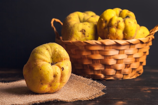 Fruit de coing naturel avec des défauts dans un panier sur une serviette en jute et un fond en bois foncé.