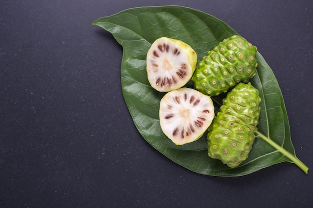 Fruit de la Grande morinda (Noni) ou Morinda citrifolia et feuille verte sur pierre noire