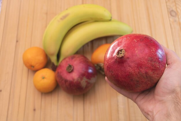 Un fruit de grenade dans la main d'un homme avec un autre mélange de fruits exotiques en arrière-plan