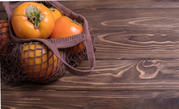 Fruit de kaki orange mûr. Gros plan de kakis frais dans un sac de ficelle sur un fond en bois. Zéro Ouest.