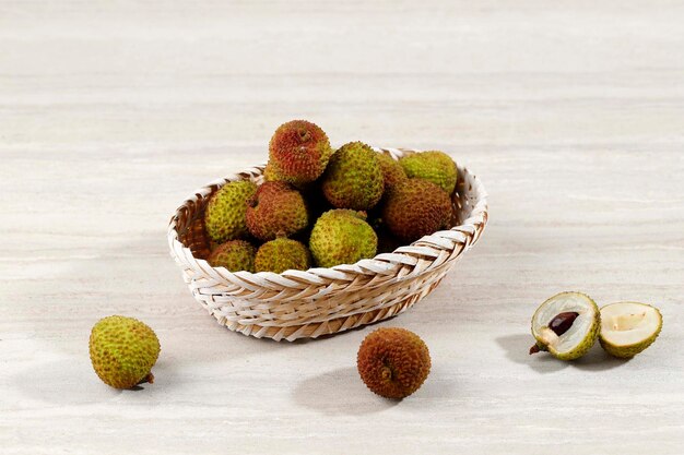 Fruit de litchi vert sur panier en rotin isolé sur table en bois