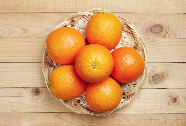 Fruit orange dans une assiette en osier sur fond de bois. Vue de dessus