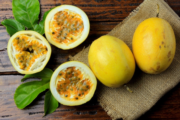 Fruit de la passion jaune avec des feuilles et coupé en deux sur des tissus de sac rustique sur une table en bois.