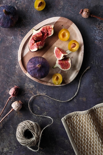 Fruits d'automne figue noire et prunes jaunes sur plateau en bois Vue de dessus à plat sur fond texturé sombre avec des plantes de pavot sèches