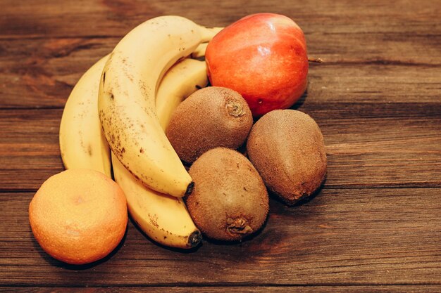 Fruits banane kiwi pomme mandarines se trouvent sur une table en bois