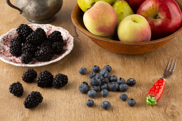 Fruits sur un bol et baies sur un plat sur une planche de bois sur une table en bois.