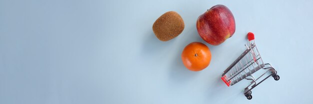 Les fruits avec un chariot de supermarché se trouvent sur fond bleu