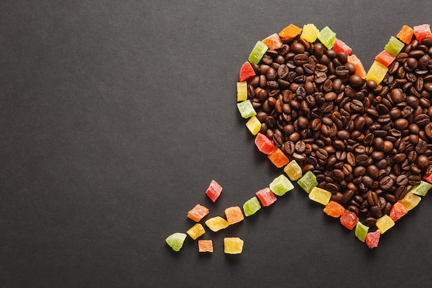 Fruits confits en forme de coeur avec flèche, grains de café bruns isolés sur fond noir pour la conception. Carte de Saint Valentin le 14 février, concept de vacances. Copiez l'espace pour la publicité.