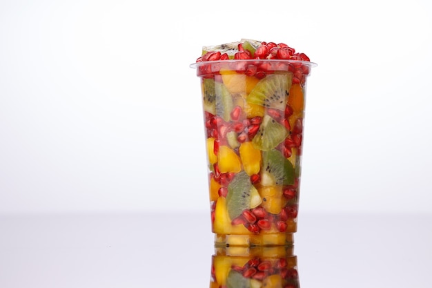 Fruits coupés mélangés disposés dans un verre transparent avec fond blanc, isolés.