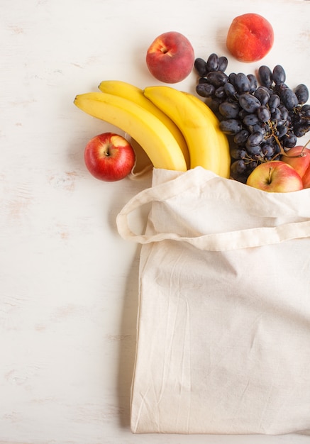 Fruits dans un sac blanc en coton réutilisable sur fond de bois blanc. Concept d'achat, de stockage et de recyclage zéro déchet. Vue de dessus, pose à plat,