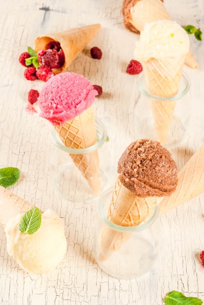 Fruits et desserts sucrés d'été, divers arômes de crème glacée dans des cônes roses (framboises), vanille et chocolat à la menthe sur du béton léger