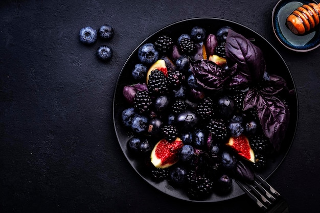 Fruits d'été bleus et noirs salade végétalienne de fruits myrtilles mûres raisins figues et basilic violet avec vinaigrette au miel sur fond sombre vue de dessus