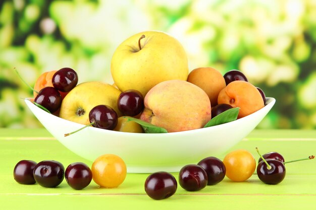 Fruits d'été brillants dans une assiette sur une table en bois sur fond naturel